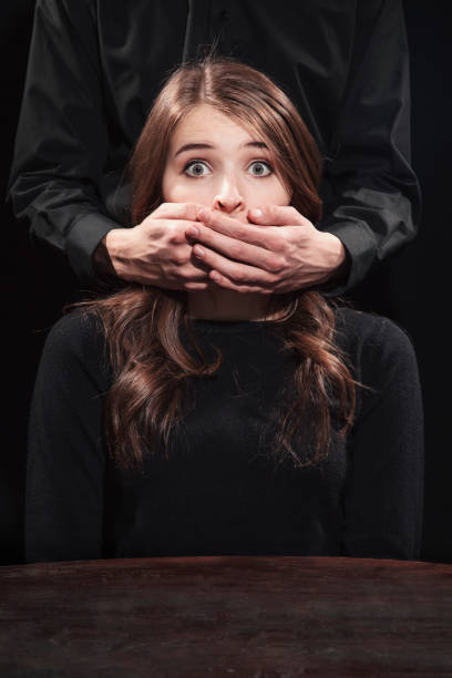 Portrait of a girl on a black background with male hands covering his mouth